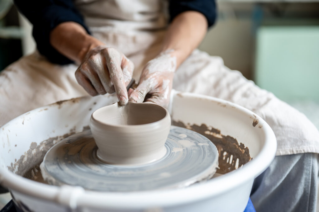 Close up pottery artist making pour spout on clay brewing bowl on throwing wheel in class or studio.