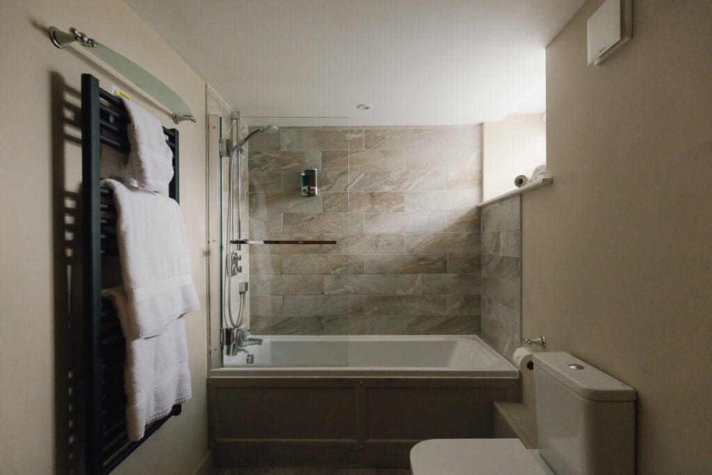 Grey bathroom tiled bath with overhead shower, toilet.
