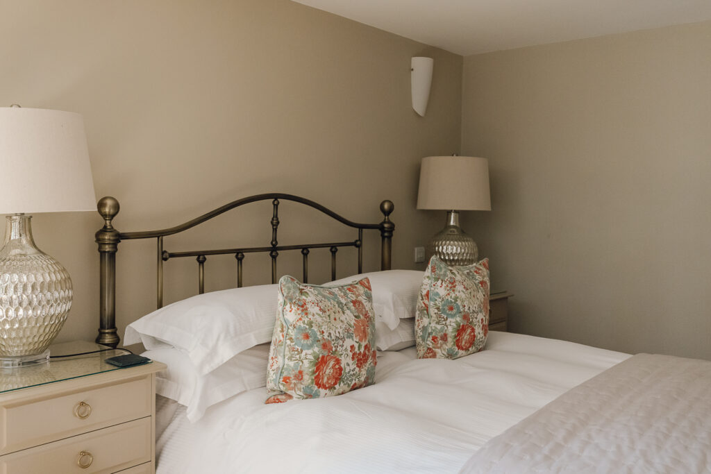Metal bed with colourful throw cushions, lamp in the corner.
