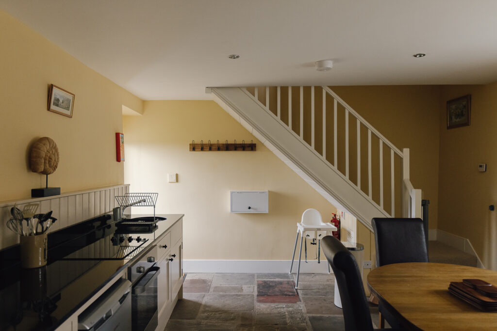 White stairs leading to upstairs. Lower floor with kitchen flags and a high chair