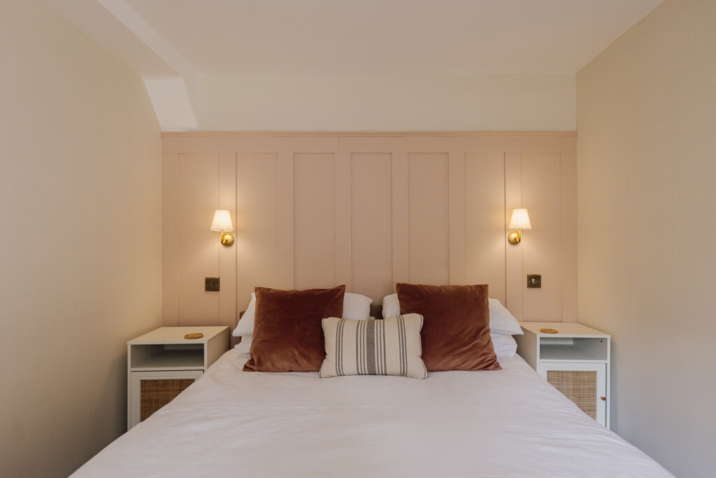 Double bed with throw pillows in front of a pink panelled wall
