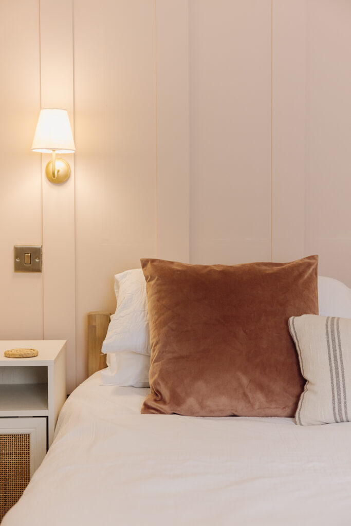 Rust throw pillow on a bed in front of pale pink panelling