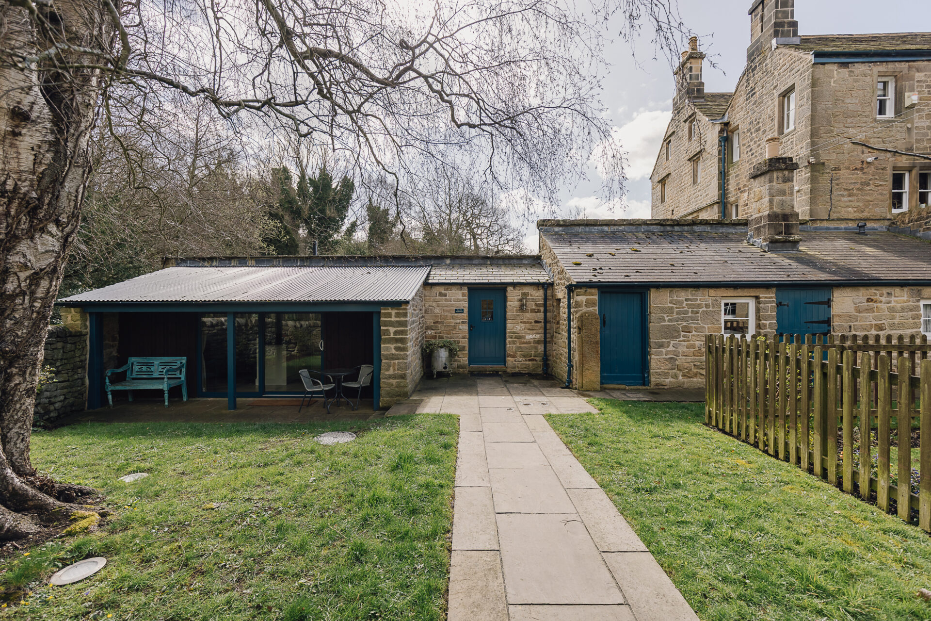 Exterior of The Old Wash House cottage with garden path, patio seating and stone buildings on the Chatsworth Estate near Bakewell