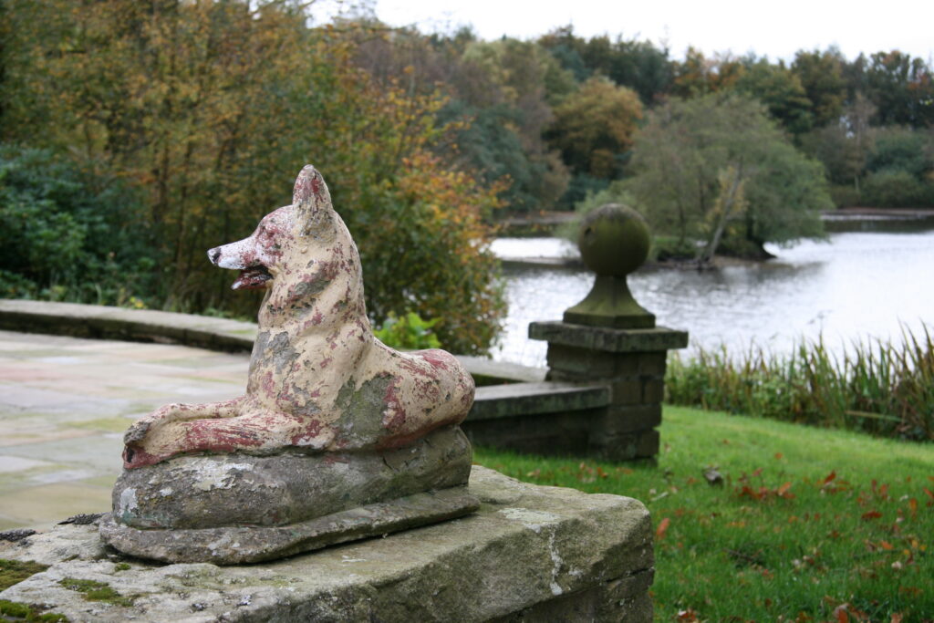 A stone statue of a dog on a paved seating area overlooking the lake.