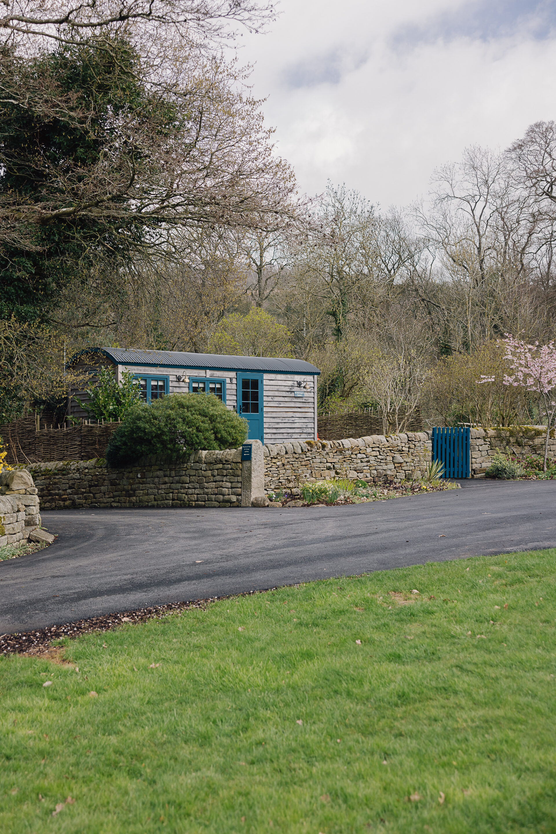 Mr McGregor’s Garden family shepherd’s hut behind a stone wall with blue gate, set in a private garden near Bakewell on the Chatsworth Estate