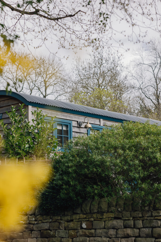 Shepherds hut set in a garden and green brush next to it