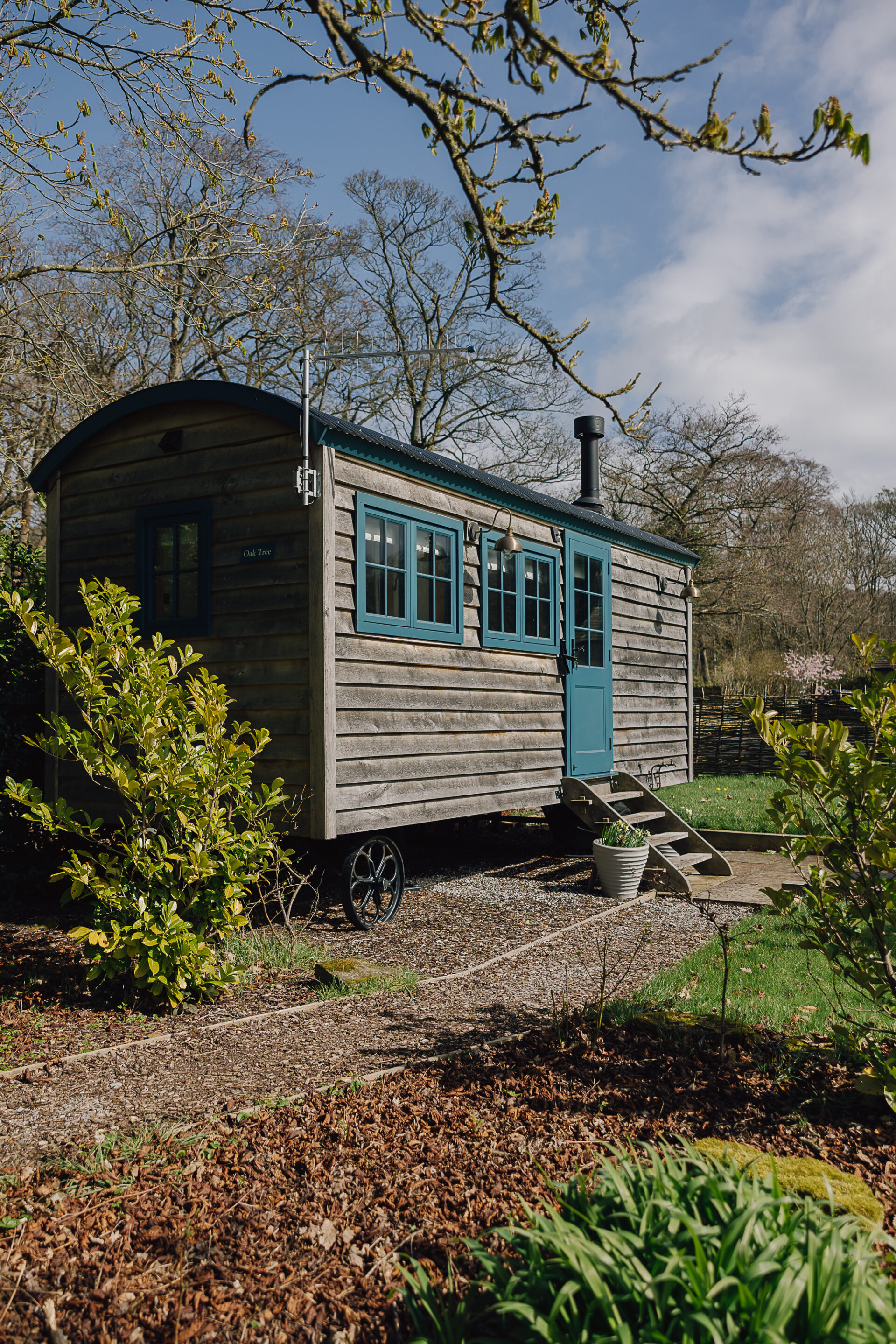 Exterior of Oak Tree shepherd’s hut with teal door, steps and garden setting, overlooking Chatsworth parkland near Bakewell