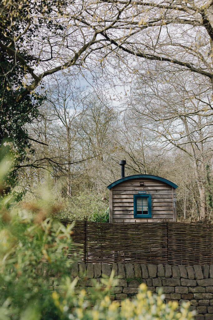 Outside of a shepherds hut with blue windows and doors, patio with bistro set for two
