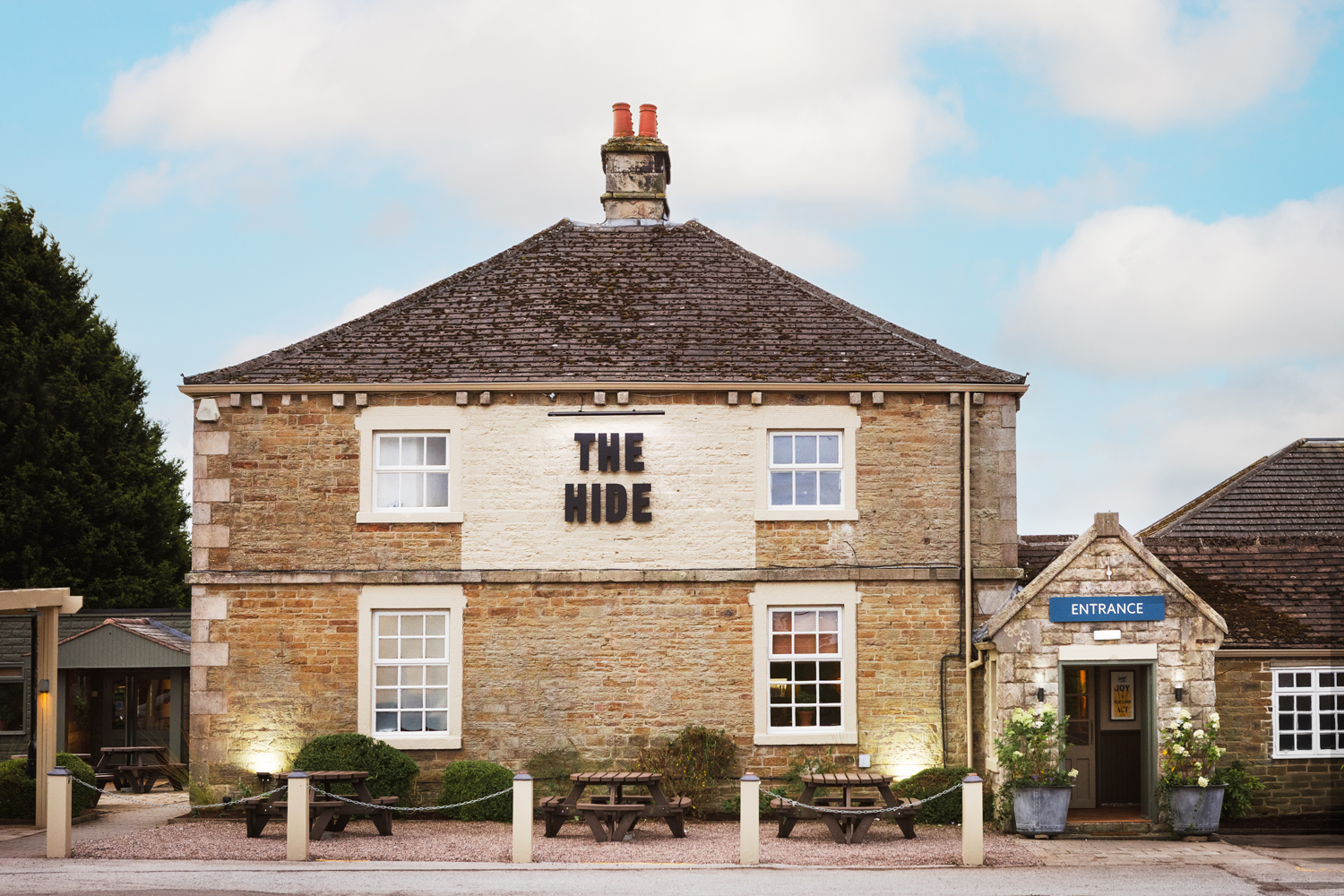 Stone exterior of The Hide Hotel near Chatsworth House, with outdoor seating at the entrance on the edge of the Peak District